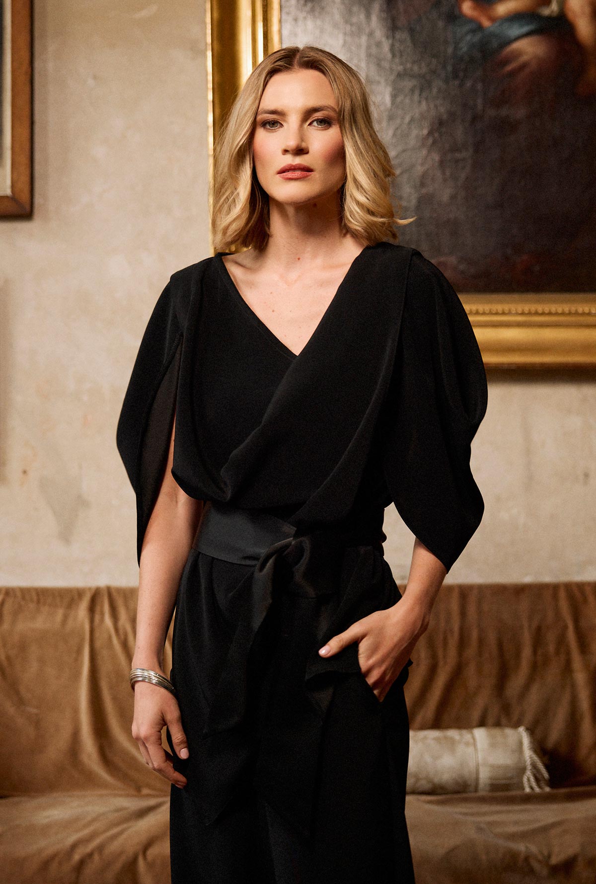Woman wearing a black outfit in an elegant room with paintings on the wall.