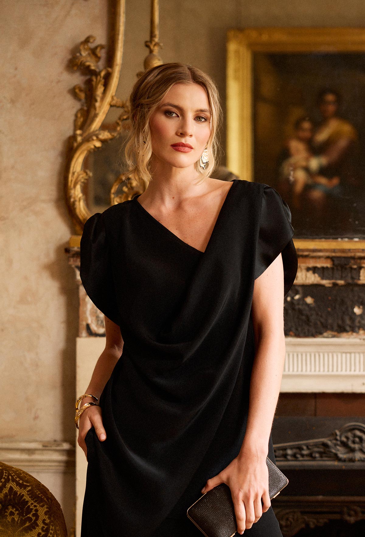 Woman in a black dress standing in an elegant room with classical decor