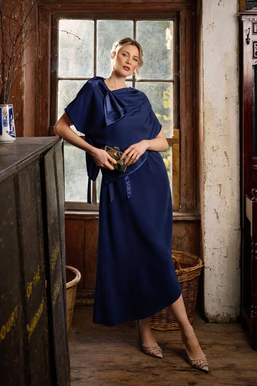 Woman in a navy blue dress standing in a room with wooden floors and a large window.