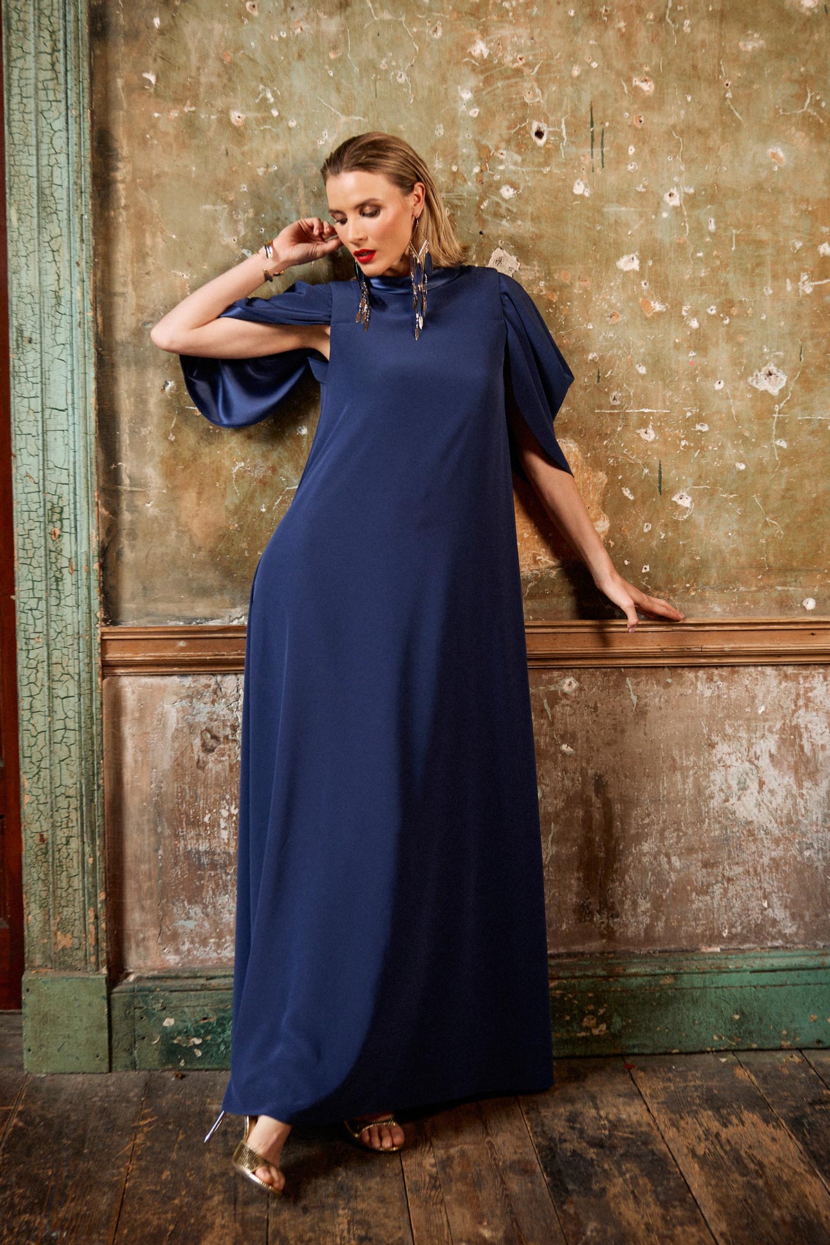 Woman in a long navy blue dress standing against an aged wall.