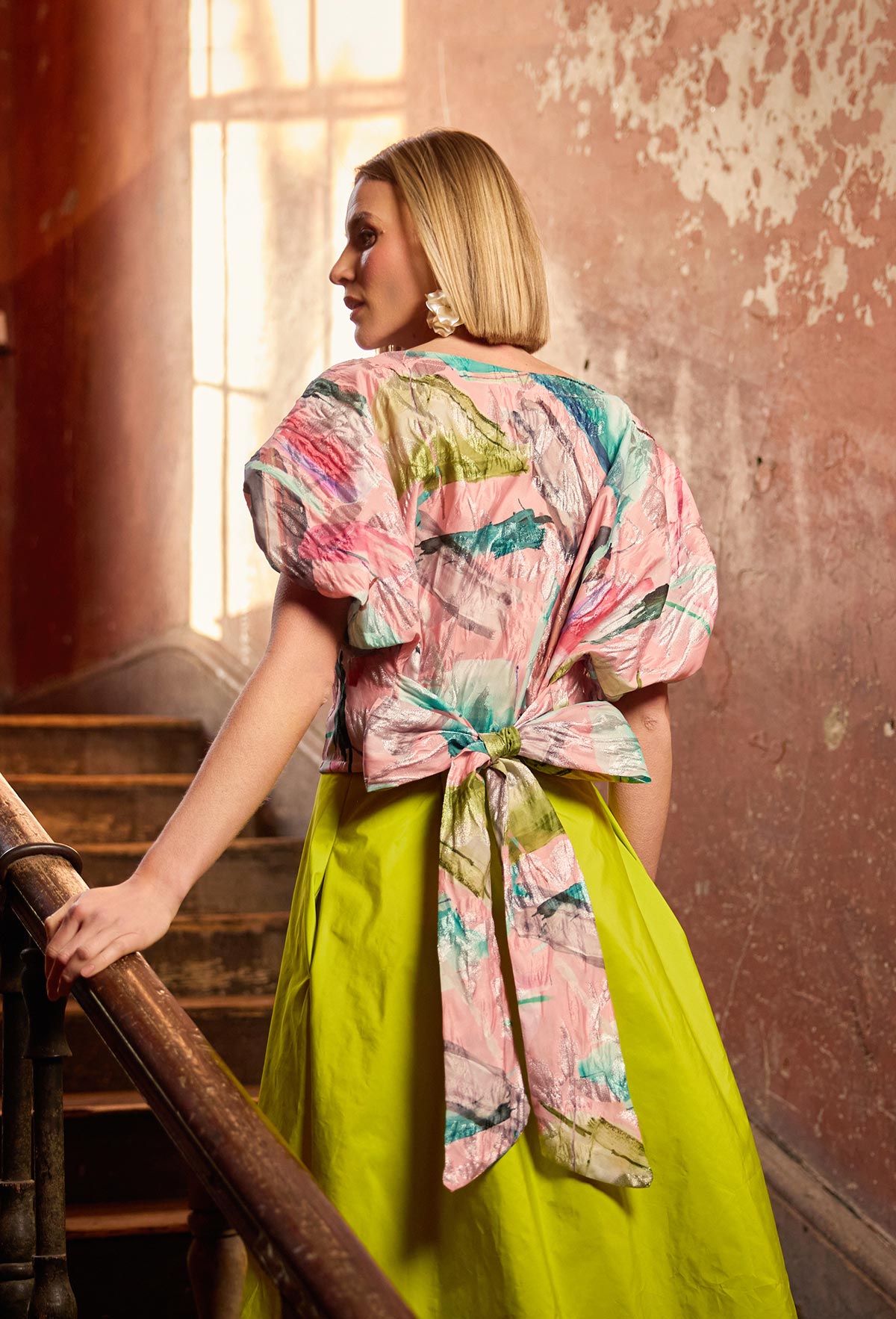 Woman wearing a colorful kimono-style top and lime
skirt in an industrial setting.