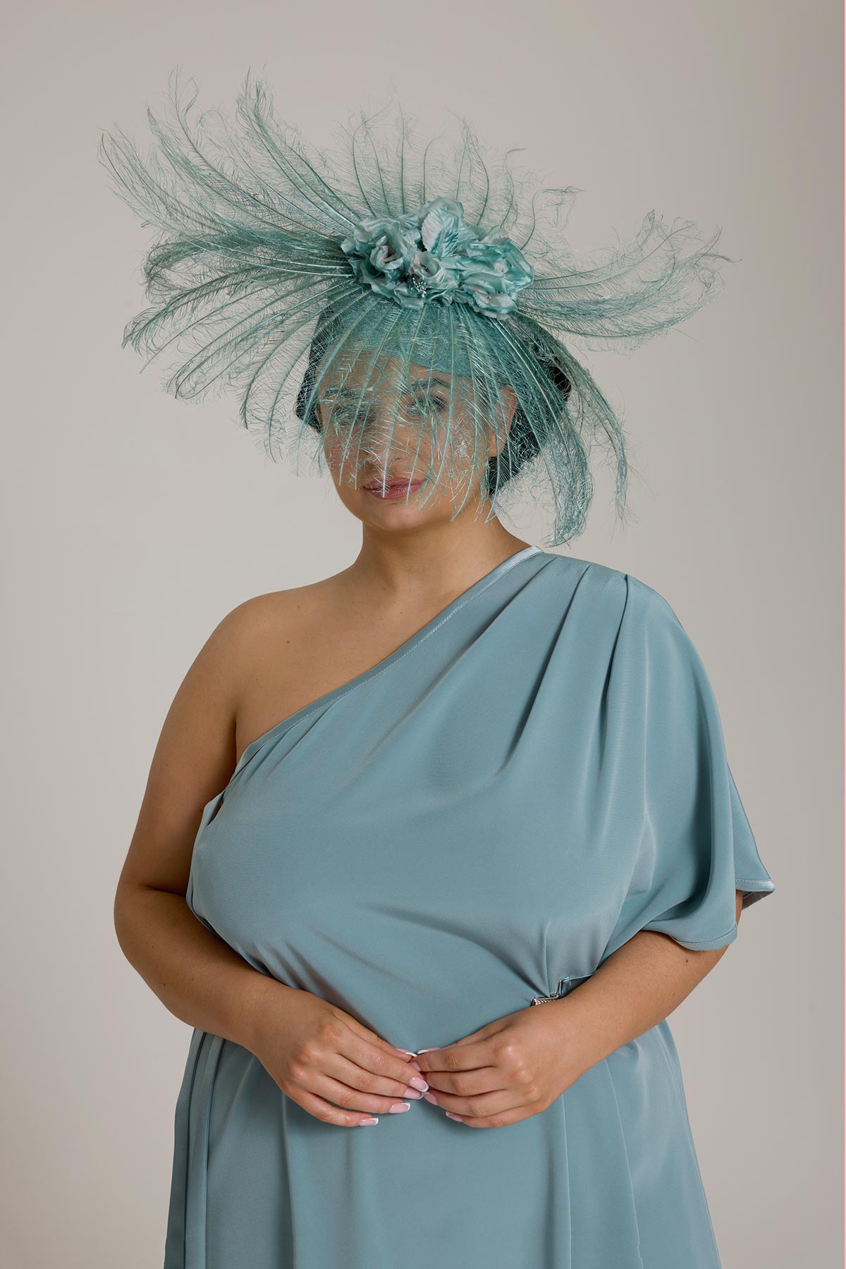 Woman in blue one-shoulder dress and elaborate feathered headpiece with matching net veil.