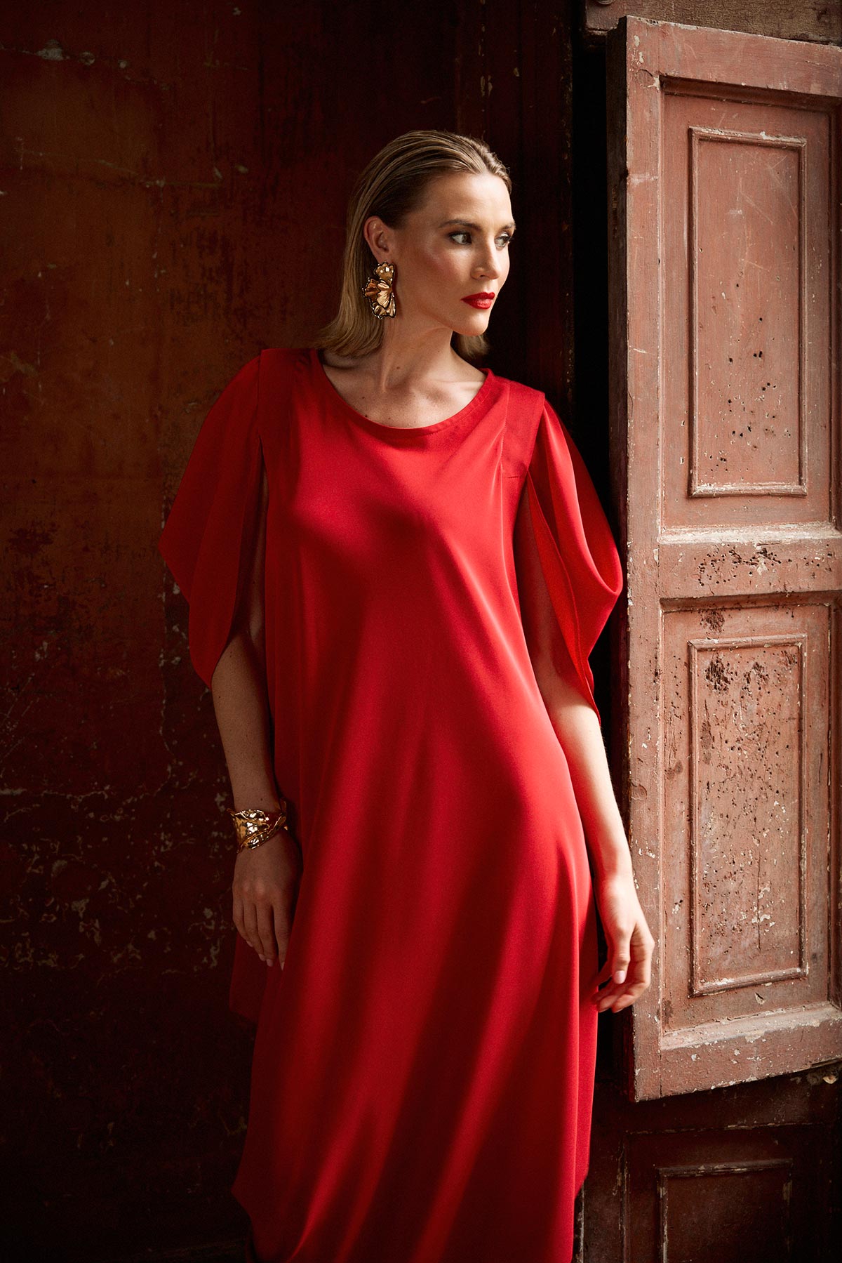 Woman in a red dress standing against a textured wall.