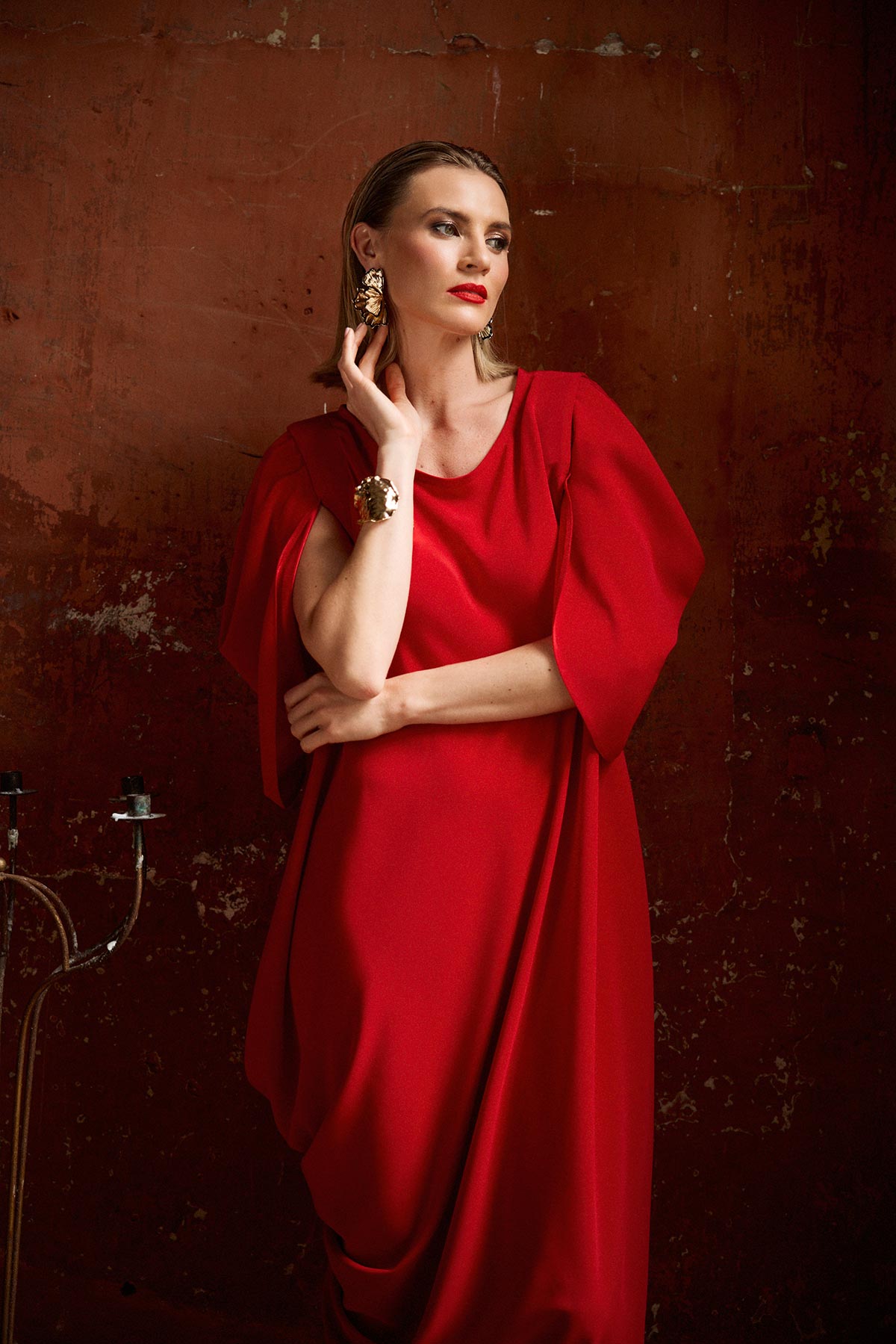 Woman in a red dress posing against a textured brown wall.