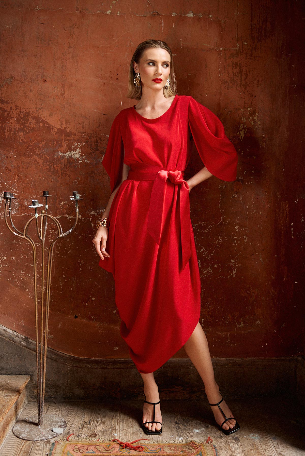 Woman in a red dress standing against a textured brown wall.