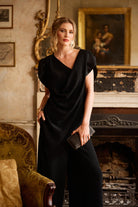 Woman in a black dress standing in an elegant room with classical decor.