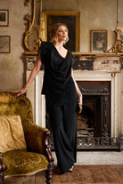 Woman in a black outfit standing in an elegant room with a fireplace and ornate furniture.