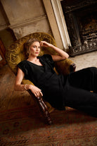 Woman in a black dress sitting on a vintage armchair in an elegant room.
