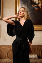 Woman in a black outfit posing in an elegant room with classical painting in the background