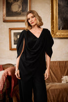 Woman wearing a black outfit in an elegant room with framed pictures on the wall.
