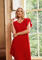 Woman in a red dress standing by a window with greenery outside
