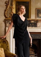 Woman in a black outfit standing in an ornate room with a fireplace.