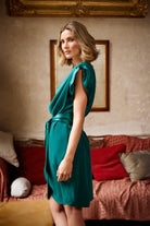 Woman in a teal dress standing in a room with a red couch and framed picture on the wall.