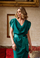 Woman in a green dress standing in an elegant room with red couch and gold frame.