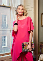 Woman in a bright pink dress holding a colorful handbag indoors.