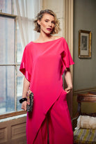 Woman in a bright pink dress standing in a room with a window and framed picture.