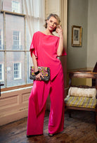 Woman in a bright pink outfit standing in a room with a window and furniture.