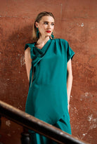 Woman wearing a teal outfit  with a large shoulder bow against a textured brown wall