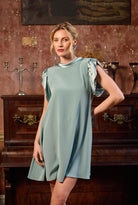 Woman in a light blue dress standing in an elegant room with wooden furniture and decorative elements.