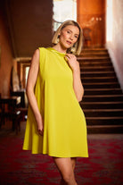 Woman in a yellow dress standing in an indoor setting with stairs and decor.