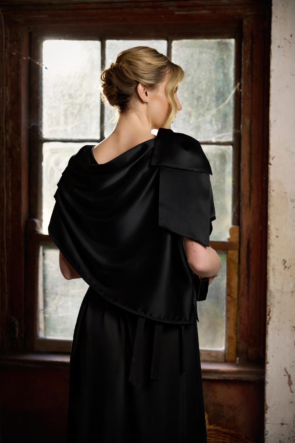 Person wearing a black dress with a draped effect in front of a window.