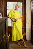 Woman in a bright yellow dress standing in a rustic interior setting.