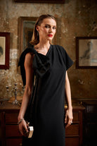 Woman in a black dress standing in an ornate room with vintage decor.