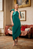 Woman in a green dress standing in an elegant room with a couch and framed portrait.