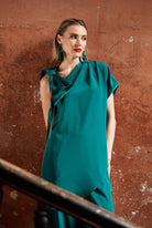 Woman wearing a teal top and trousers  against a textured brown wall