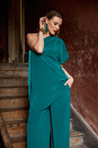 Woman in a teal top and trousers  standing on steps with a brown wall background