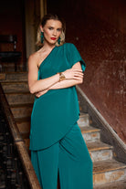 Woman in a teal top and trousers  standing on a staircase with a textured wall background