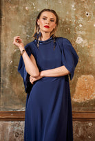 Woman wearing a blue dress against a textured wall.