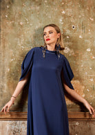 Woman wearing a blue dress against a textured wall.
