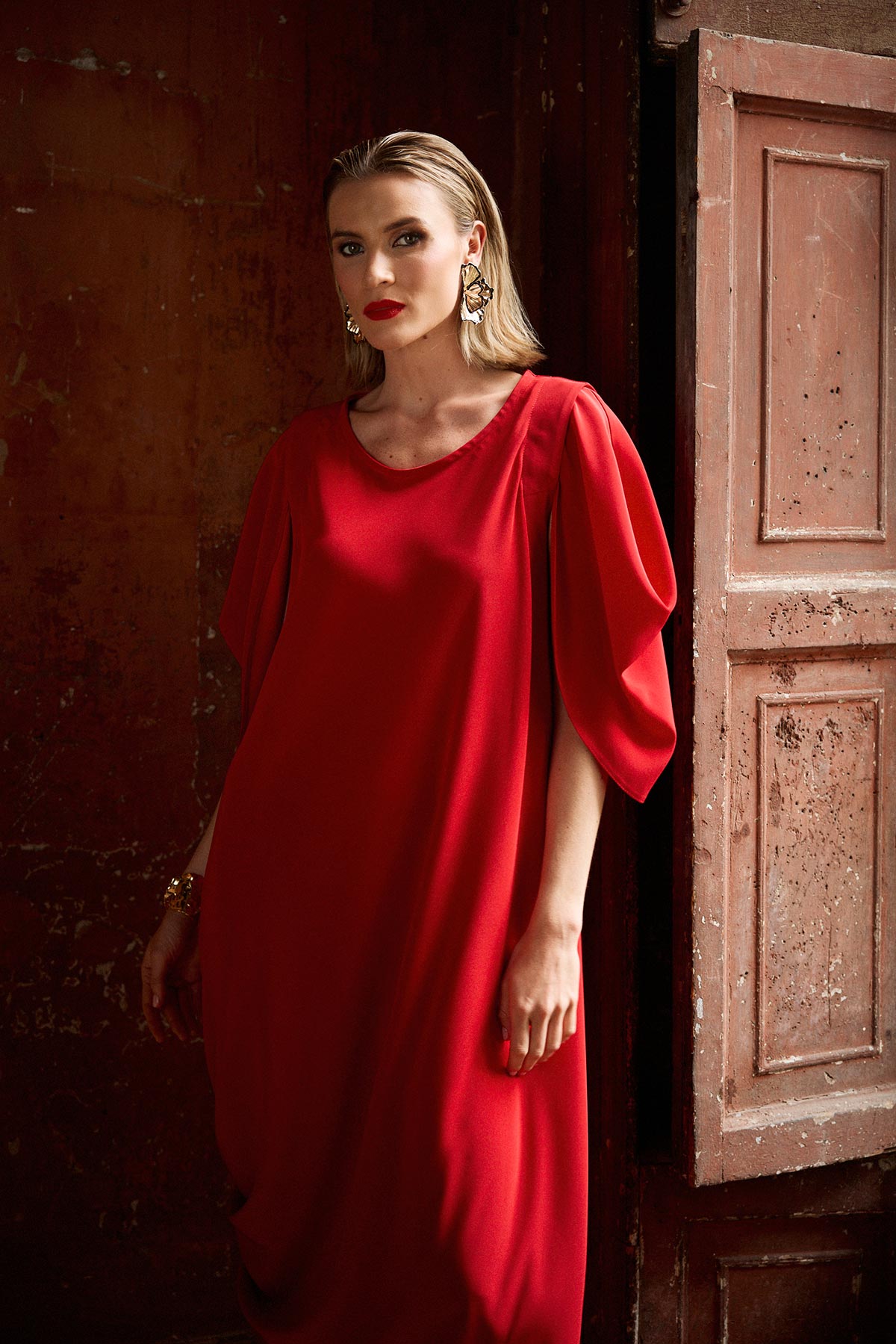 Woman in a red dress standing against a textured wall.