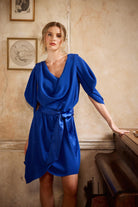 Woman in a blue dress standing in a room with framed pictures on the wall.