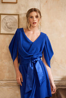 Woman wearing a blue dress against a beige wall.