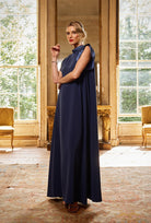 Woman in a long navy dress standing in an elegant room with large windows.