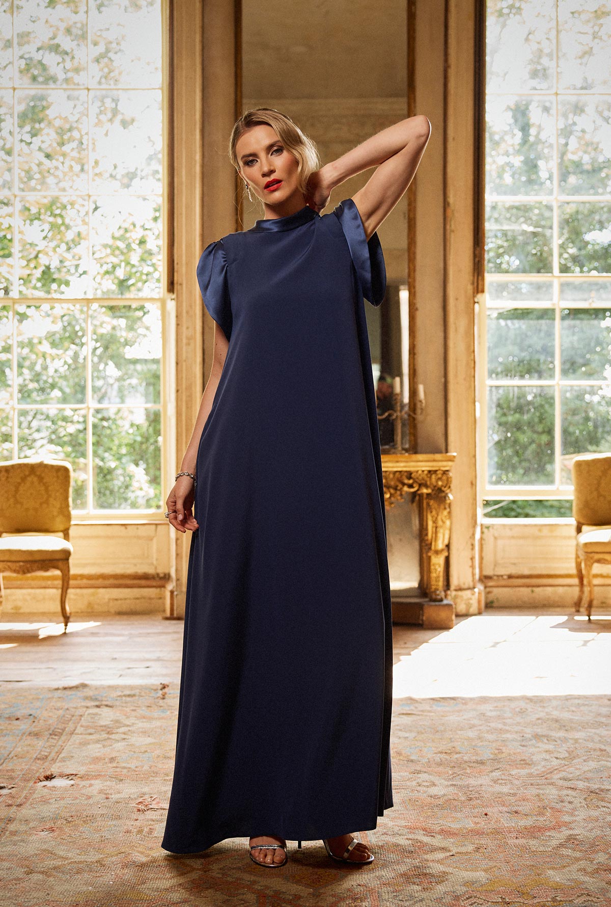 Woman in a navy blue dress standing in an elegant room with large windows.