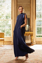 Woman in a long navy dress standing in a room with large windows and a mirror.