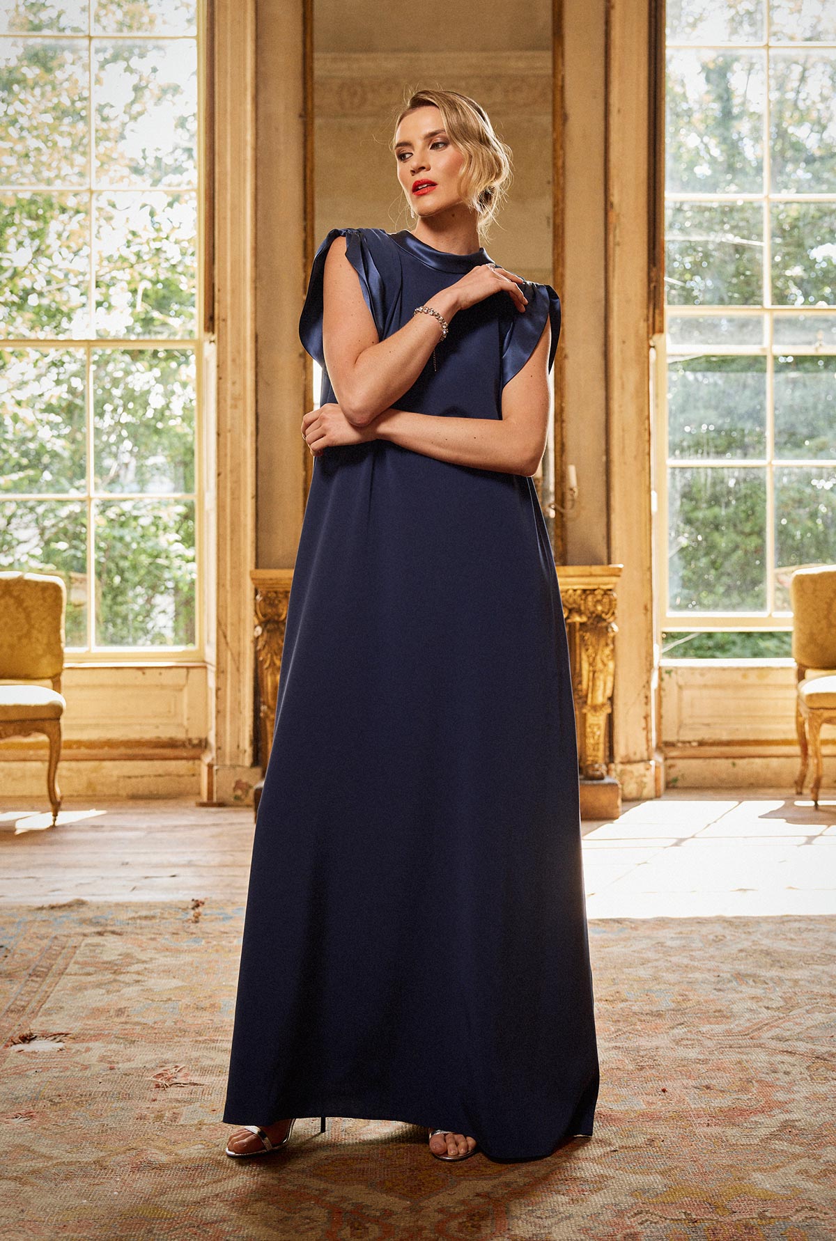 Woman in a navy blue dress standing in an elegant room with large windows.