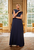 Woman in a navy blue dress standing in an elegant room with large windows.