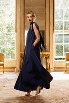 Woman in a navy blue dress standing in an elegant room with large windows.