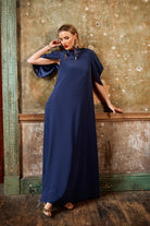 Woman in a long navy blue dress standing against an aged wall.