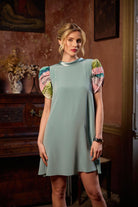 Woman wearing a light blue dress with colorful sleeves in an indoor setting.