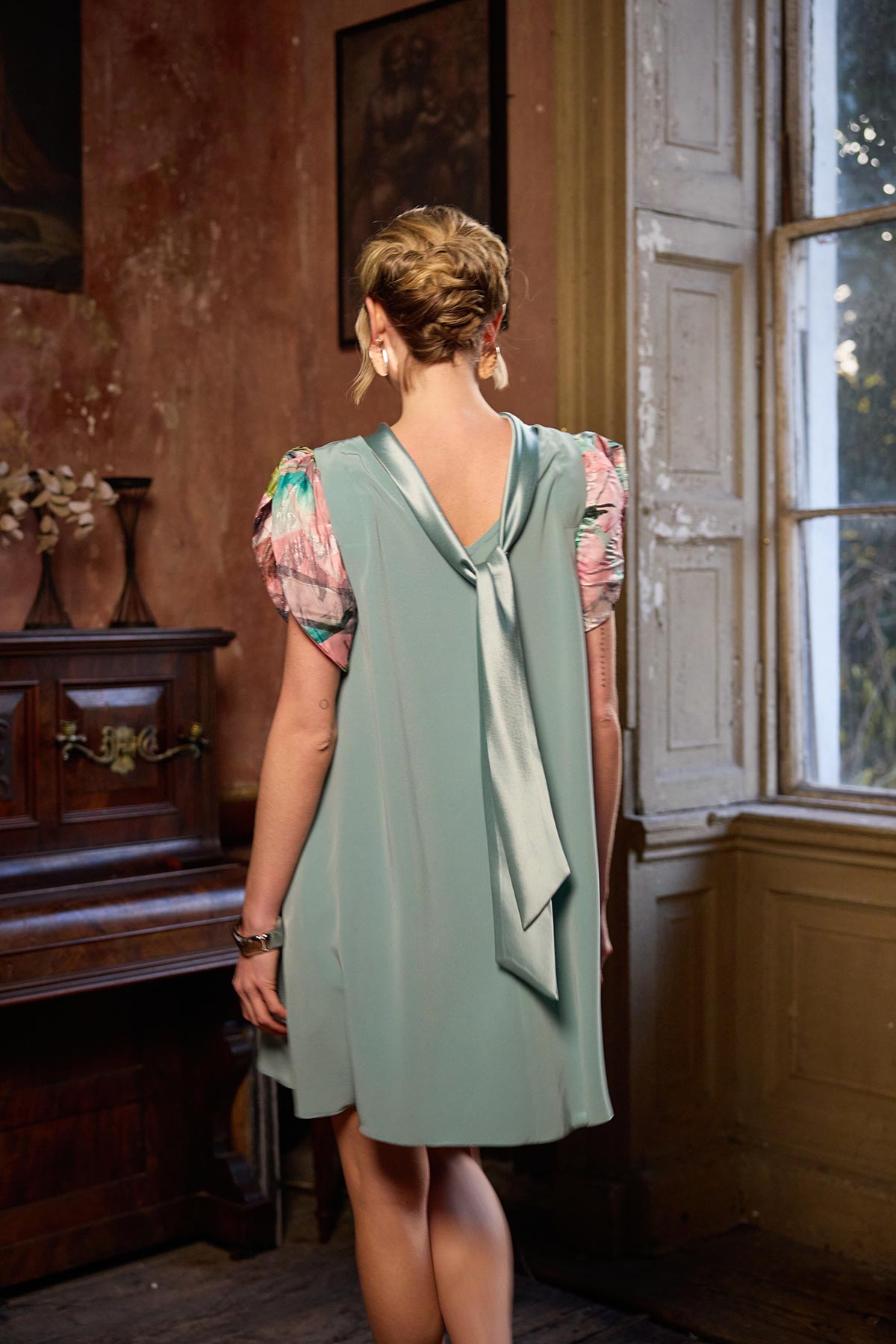 Woman wearing a light green dress with a pink blouse in an old-fashioned room.