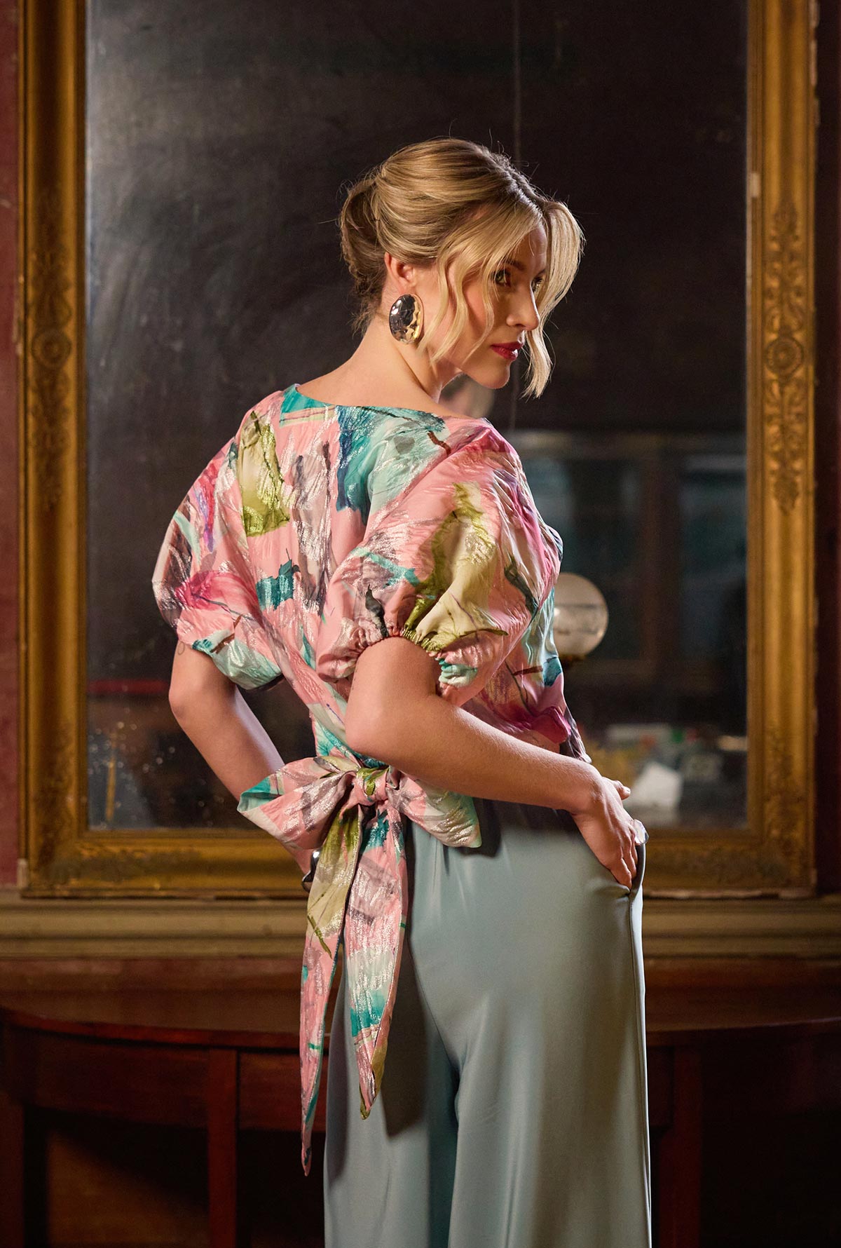 Woman wearing a floral kimono-style top and light-colored pants in an ornate room.