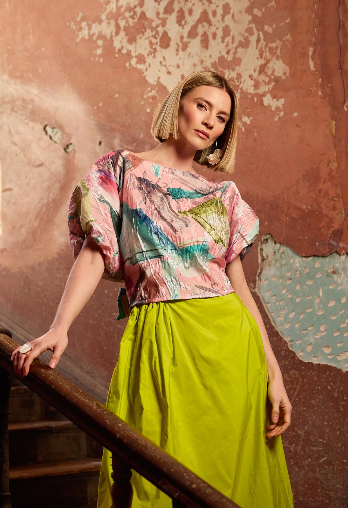 Woman wearing a colorful top and lime colour skirt against a textured wall.