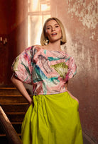 Woman wearing a colorful top and lime skirt in an indoor setting with textured walls.