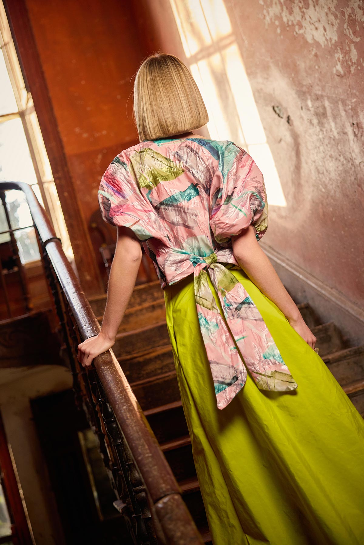 Person wearing a colorful top and lime skirt standing on a staircase.