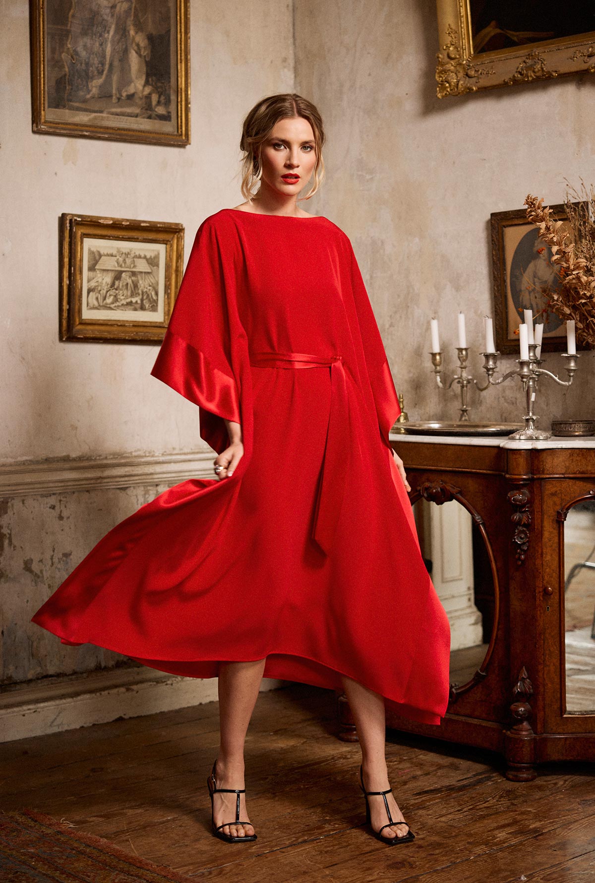 Woman in a red dress standing in an elegant room with classical decor.